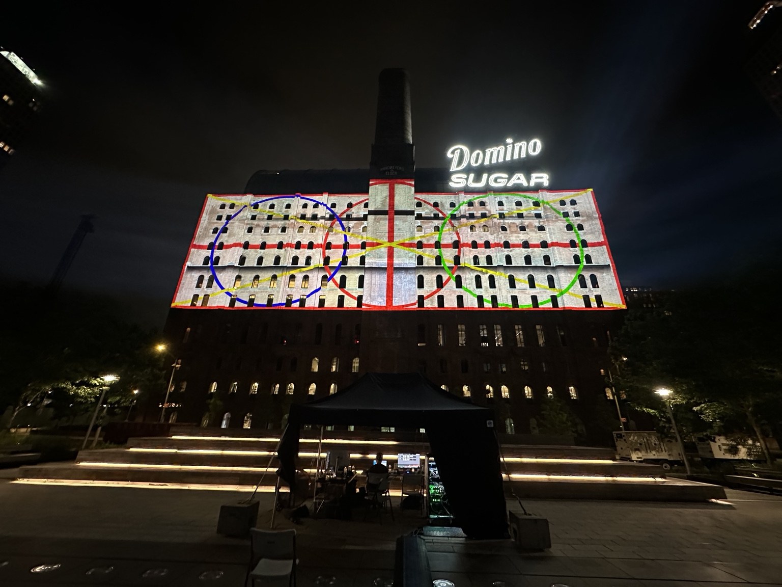 A geometric calibration test pattern projected across the Domino Sugar building at night.