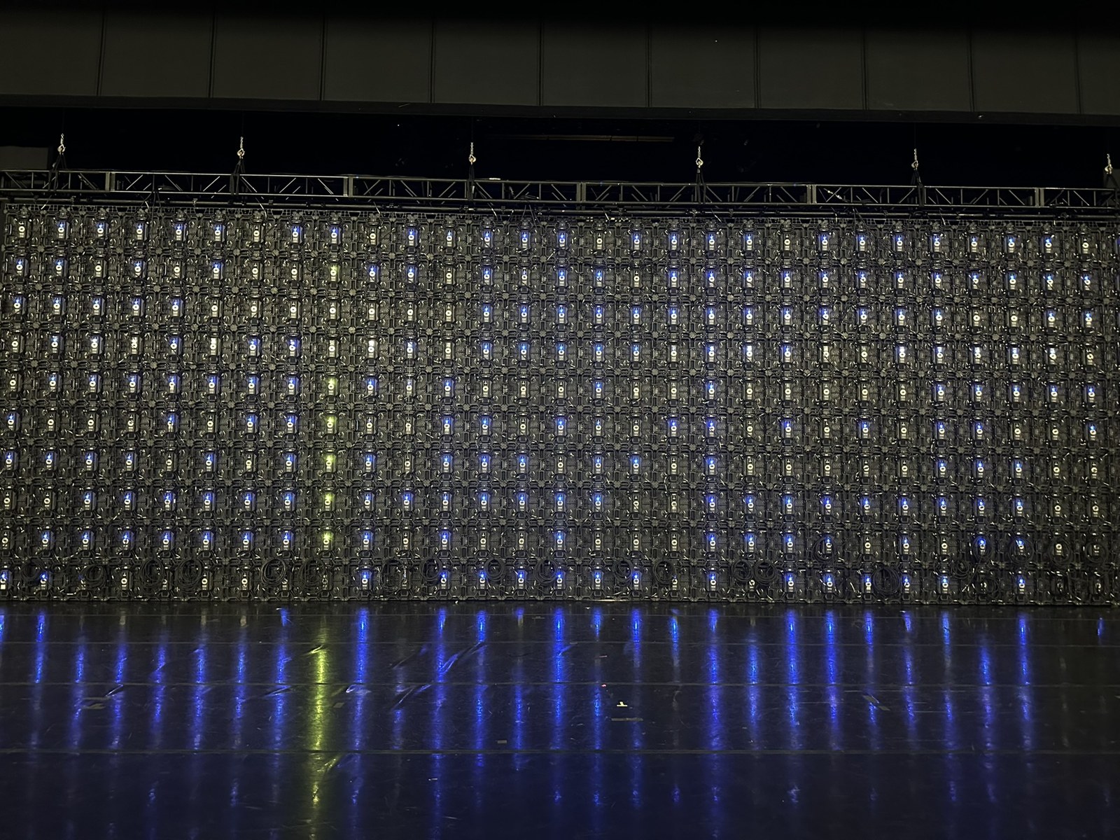 Rear of a large LED wall, with repeating panel electronics and blue indicator lights reflected on the floor.