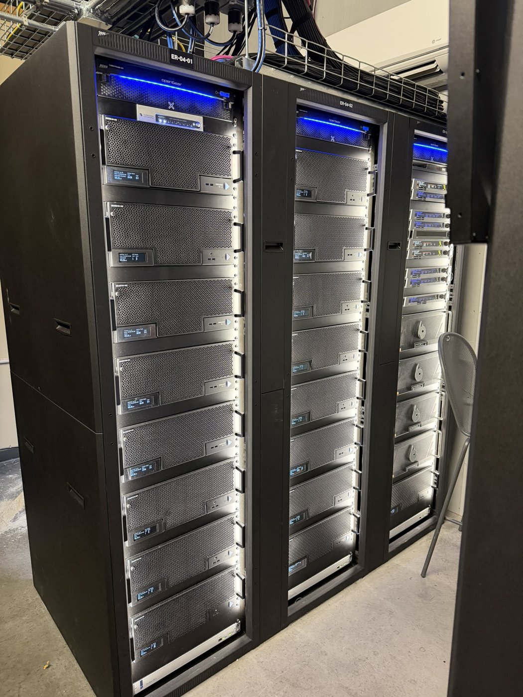 Three tall server racks with equipment installed behind glass doors.