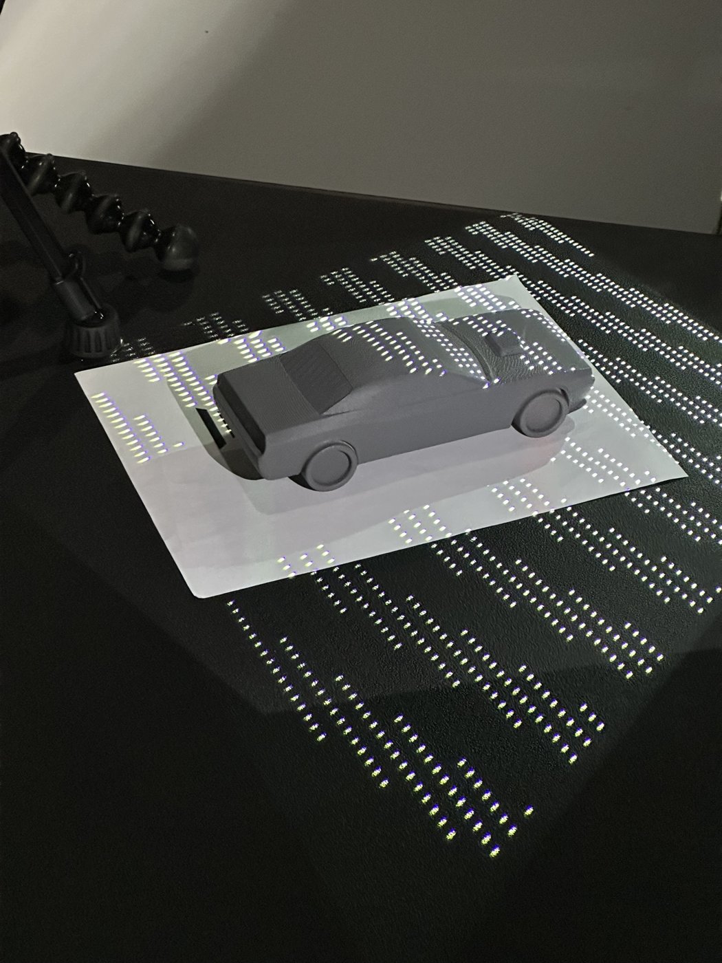 A small model car on a table surrounded by a projected alignment pattern.