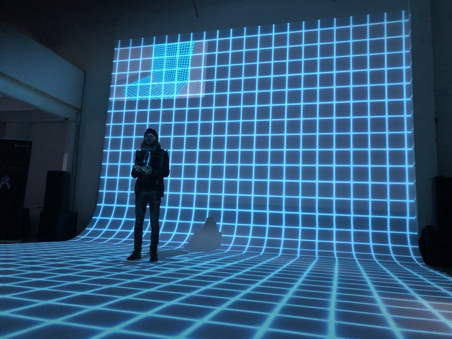 Tatton presenting a training session in front of a blue calibration grid projected across a curved wall and floor.